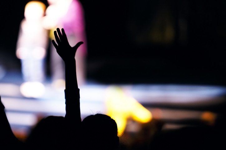 Supporter in the audience raising a hand at a live performance silhouetted against the blurred outline of people on stage