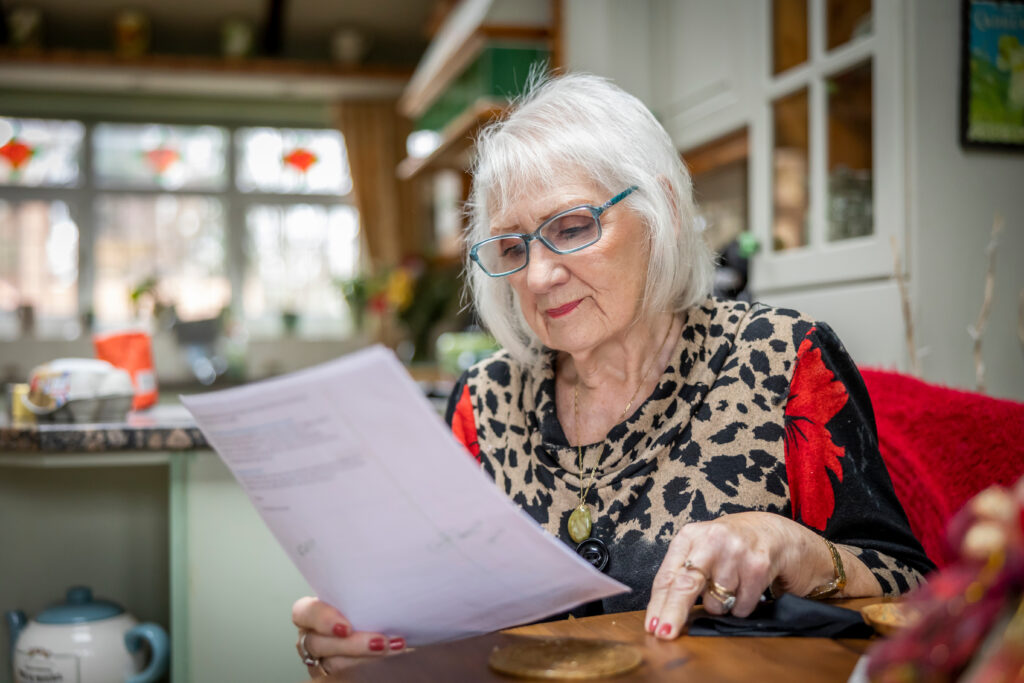 Woman (representative of independent self-funders), reviewing paperwork at her kitchen table. 