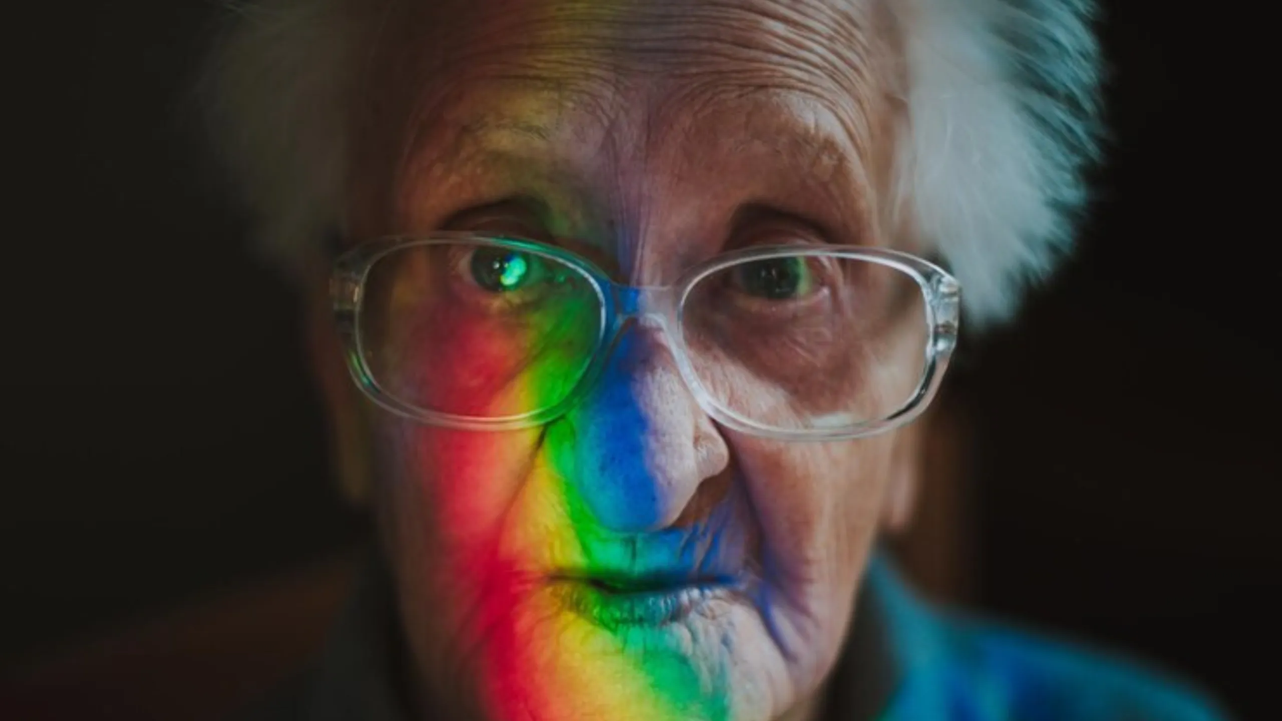 Elderly man with a rainbow reflecting on his face - official press photo for At the Rainbow's End